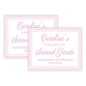 May include: Two pink and white gingham patterned signs with the text "Caroline's First Day of Second Grade" and "Caroline's Last Day of Second Grade Goldsmith Schiffman 2023-2024" in pink cursive font.