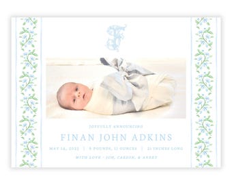 May include: A baby announcement card with a blue and white floral border. The card features a photo of a baby boy wrapped in a white blanket. The text on the card reads "Joyfully announcing Finan John Adkins May 14, 2023 6 pounds, 11 ounces 21 inches long With love - Jon, Carson, & Avery"