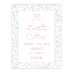 Op de afbeelding: Een rechthoekige kaart met een witte achtergrond en een bloemenpatroon in roze, blauw en groen. De kaart bevat de naam "Lucille Collins" in roze script, samen met andere tekst, waaronder "Goldsmith-Schiffman" en "3rd Grade."