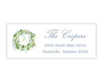 Pode incluir: Uma etiqueta retangular branca com um design de coroa de flores em aquarela e texto. A coroa apresenta folhas verdes, bagas azuis e fitas creme. O texto diz "The Coopers" e um endereço em Huntsville, Alabama.