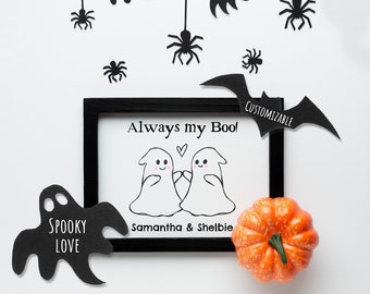 Może przedstawiać: Czarny obraz w ramie z tekstem "Always my Boo!" i dwoma kreskówkowymi duchami trzymającymi się za ręce. Tekst "Samantha & Shelbie" znajduje się pod duchami. Obraz jest otoczony czarnymi papierowymi nietoperzami, pająkami i duchami.