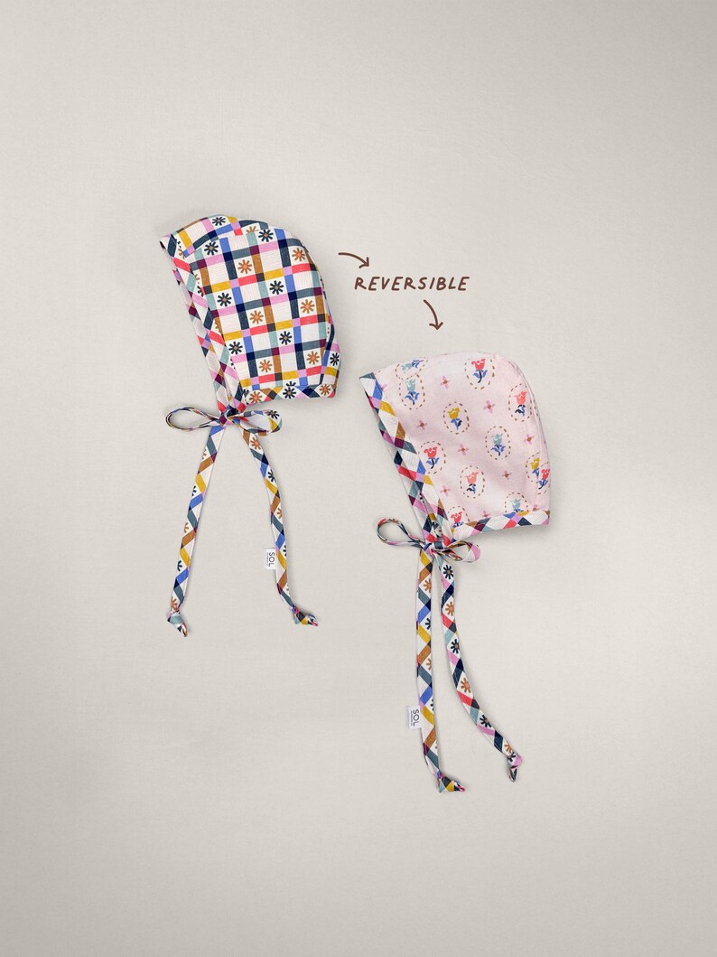 Reversible brimless baby bonnet, showing gingham side and floral side laid flat, handmade from organic cotton