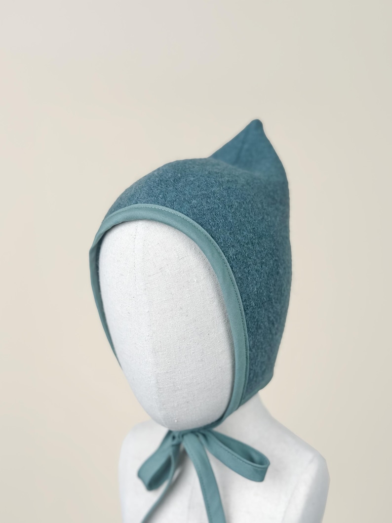 Close-up angled view of Juniper boiled wool pixie bonnet highlighting wool texture and bias trim.