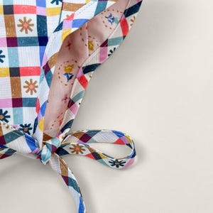 Close-up of reversible baby bonnet showing contrast binding, chin tie, and organic cotton fabric details