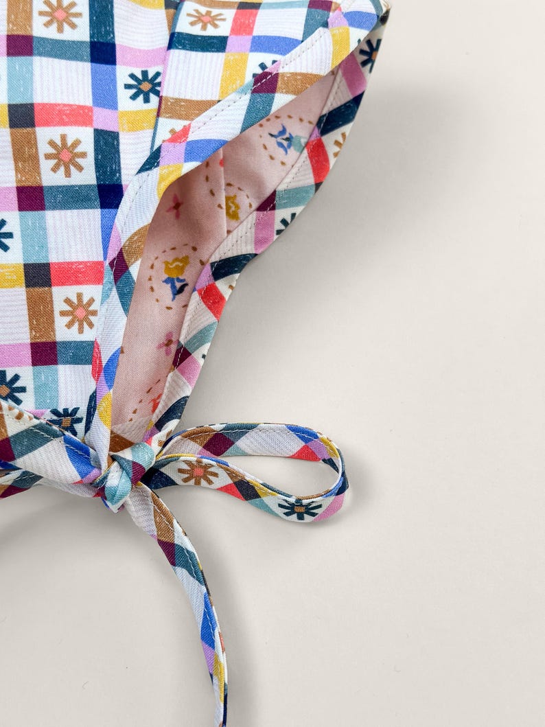 Close-up of reversible baby bonnet showing contrast binding, chin tie, and organic cotton fabric details