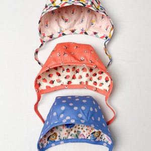 Stack of three reversible baby & toddler bonnets in various prints and colors, showing variety and lining details.