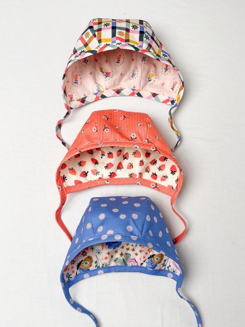 Stack of three reversible baby & toddler bonnets in various prints and colors, showing variety and lining details.