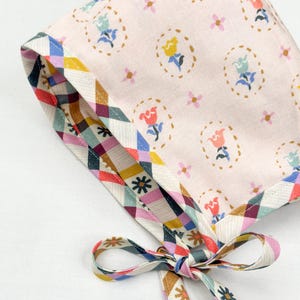 Angled view of the bonnet with the pink floral side out and gingham floral trim visible along the edges and ties.