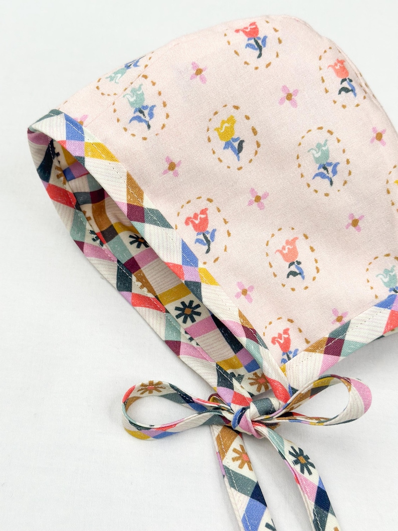 Angled view of the bonnet with the pink floral side out and gingham floral trim visible along the edges and ties.