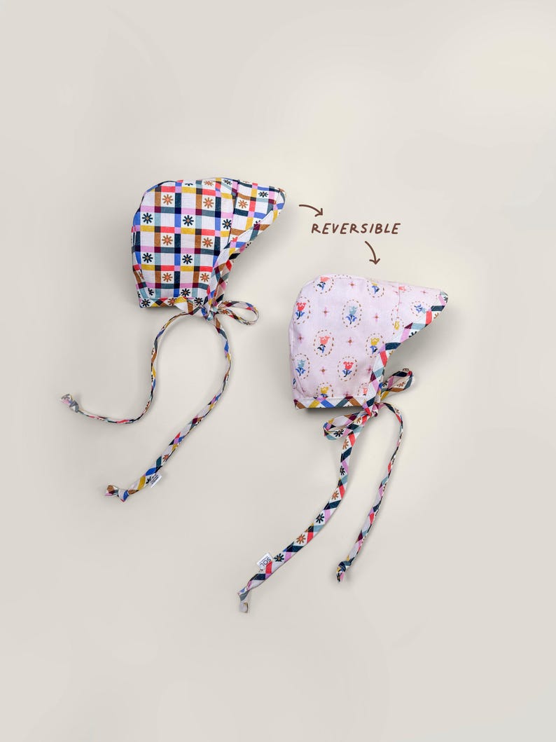 Reversible baby bonnet with brim, showing gingham side and floral side laid flat, handmade from organic cotton