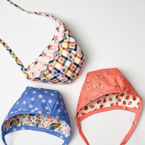 Three reversible baby & toddler bonnets with different prints, including coral floral and strawberry designs, laid flat.