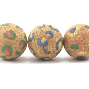 May include: Three cork balls with a colourful abstract pattern. The balls are painted with yellow, blue, green, and pink.