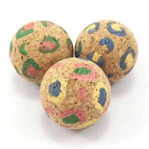 May include: Three cork balls with colourful painted patterns. The patterns include green, blue, yellow, and pink.