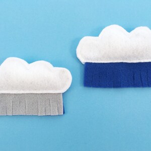 May include: Two felt cloud shapes with fringe details. The cloud on the left has grey fringe and the cloud on the right has blue fringe.