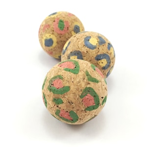 May include: Three cork balls with a leopard print design painted on them. The balls are painted in shades of green, pink, yellow, and blue.