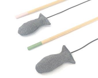 May include: Cat toys with a fish-shaped head made of grey fabric attached to a wooden stick. The ends of the sticks are painted in pastel pink and green. The toys are designed for cats.
