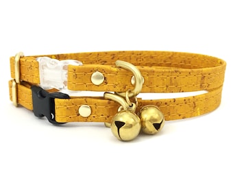 Peut inclure: Un collier de chat en liège jaune avec une boucle noire et deux cloches dorées.