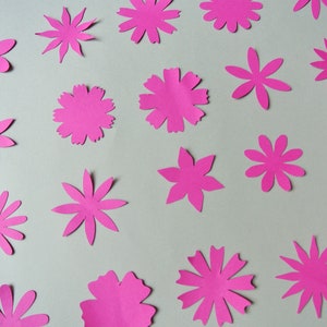 May include: A collection of 17 pink paper flowers of various sizes and shapes, cut out and arranged on a white background.