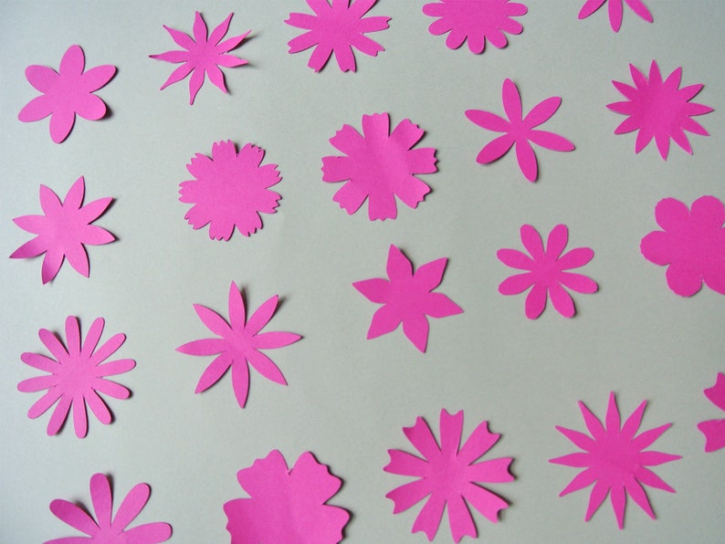 May include: A collection of 17 pink paper flowers of various sizes and shapes, cut out and arranged on a white background.