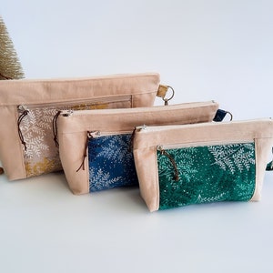 May include: Three beige zippered pouches with different patterned fabric inserts. The largest pouch has a yellow and white floral pattern, the middle pouch has a blue and white floral pattern, and the smallest pouch has a green and white floral pattern.