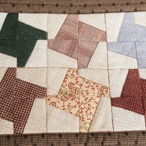 May include: A brown quilted hot pad with a patchwork design featuring six different fabric patterns in shades of brown, green, red, beige, and grey. The hot pad has a brown border with white polka dots.