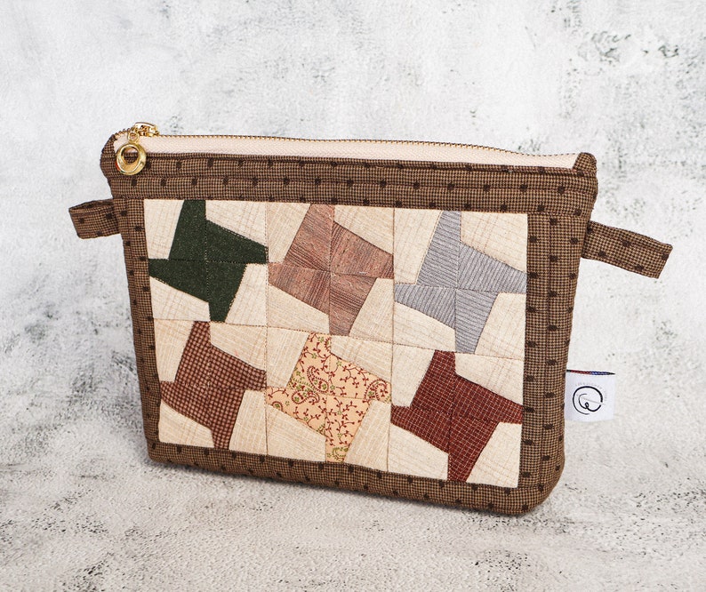 May include: A brown zippered pouch with a patchwork design featuring various shades of brown, green, and red. The pouch has a brown polka dot pattern on the border.
