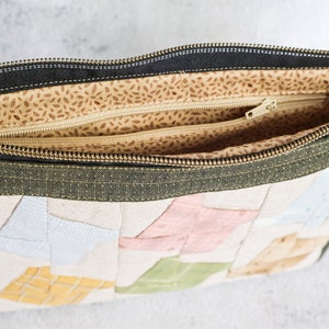 May include: A green zippered pouch with a patchwork design of colourful fabric squares. The pouch is open and the inside is lined with a beige fabric with brown speckles.