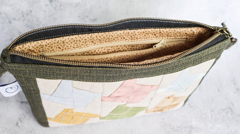 May include: A green zippered pouch with a patchwork design of colourful fabric squares. The pouch is open and the inside is lined with a beige fabric with brown speckles.