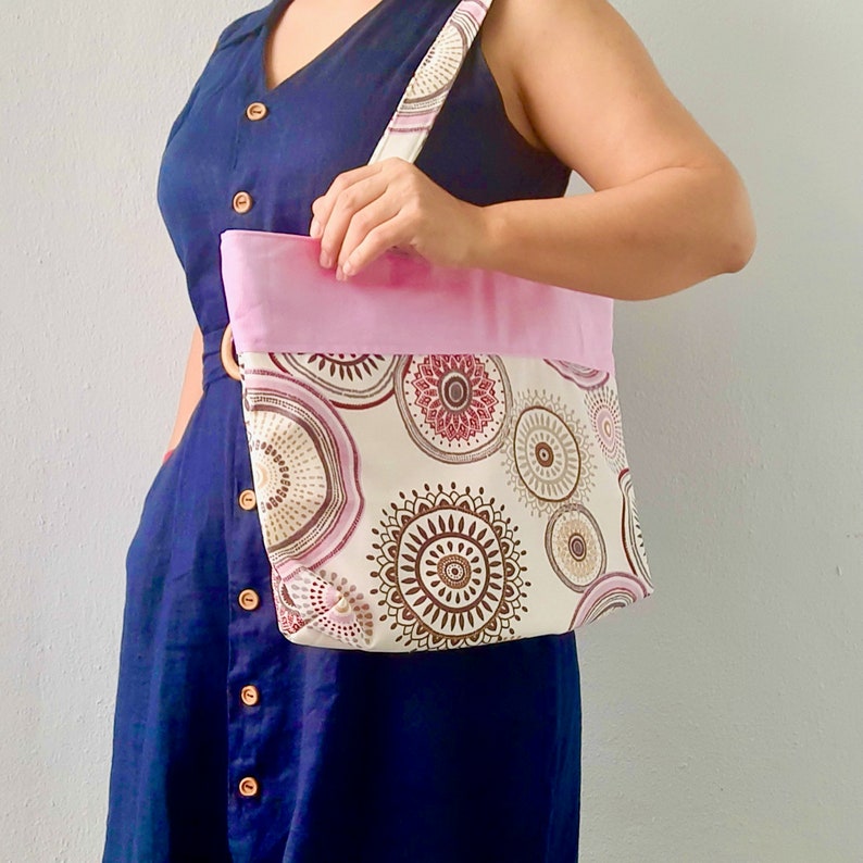 Peut inclure: Un sac cabas rose et blanc avec un motif mandala brun et rose. Le sac est doubl&eacute; de tissu rose et poss&egrave;de une anse en cuir marron.