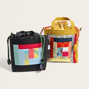 May include: Two drawstring bags with patchwork designs. One is black with a colourful geometric pattern, green drawstring, and a small handle. The other is mustard yellow with a patchwork design, red drawstring, and a yellow handle.
