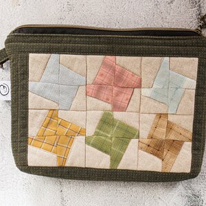 May include: A green zippered pouch with a patchwork design. The patchwork is made of different coloured fabrics, including blue, pink, yellow, and green. The pouch has a zipper closure and a small handle.