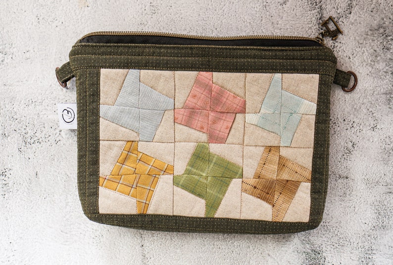 May include: A green zippered pouch with a patchwork design. The patchwork is made of different coloured fabrics, including blue, pink, yellow, and green. The pouch has a zipper closure and a small handle.