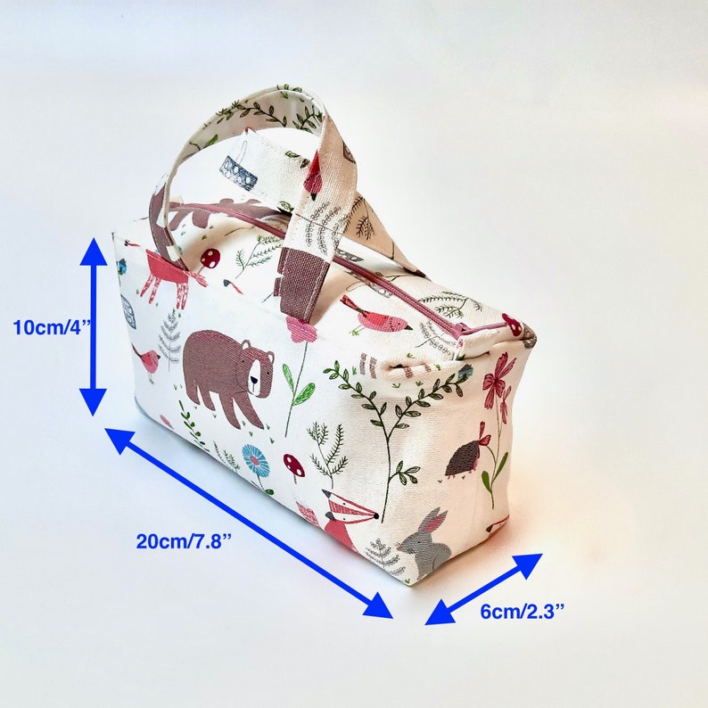 May include: A white canvas tote bag with a woodland animal print featuring bears, birds, foxes, and rabbits. The bag has a brown handle and measures 7.8 inches wide, 4 inches tall, and 2.3 inches deep.