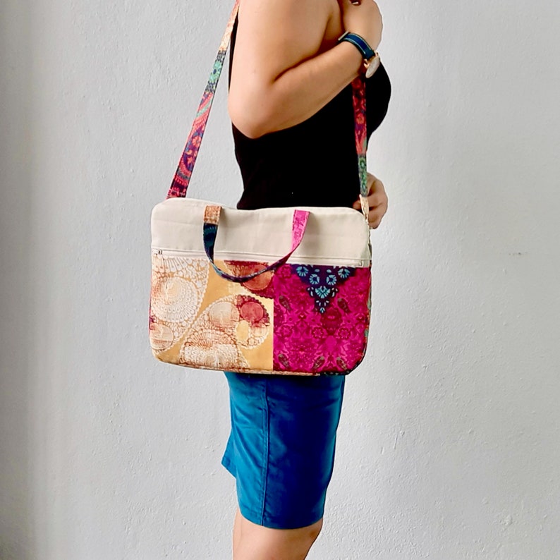 K&ouml;nnte beinhalten: Eine mehrfarbige Patchwork-Tragetasche mit beigefarbener Canvas-Basis und Rei&szlig;verschluss. Die Tasche wird &uuml;ber der Schulter getragen und hat einen langen Riemen.