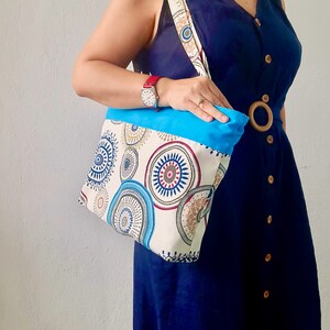Peut inclure: Un sac cabas bleu et blanc avec un motif g&eacute;om&eacute;trique color&eacute;. Le sac est doubl&eacute; de tissu bleu et poss&egrave;de une poign&eacute;e en bois brun.