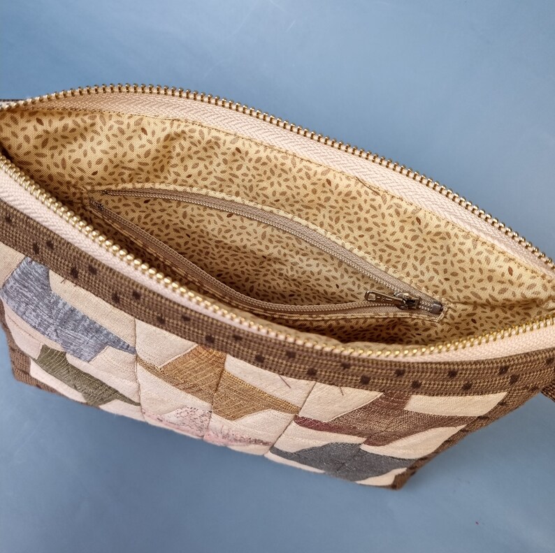 May include: A brown and beige patchwork fabric zipped pouch with a beige fabric lining and a zipped pocket inside.