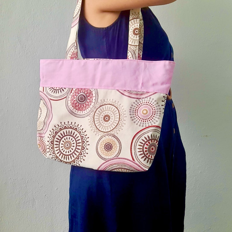 Peut inclure: Un sac cabas rose et blanc avec un motif mandala brun et rose. Le sac a un dessus en tissu rose et deux longues lani&egrave;res.