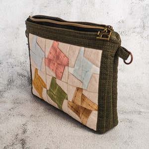 May include: A green quilted zippered pouch with a patchwork design featuring various colours and patterns. The pouch has a brown leather strap.