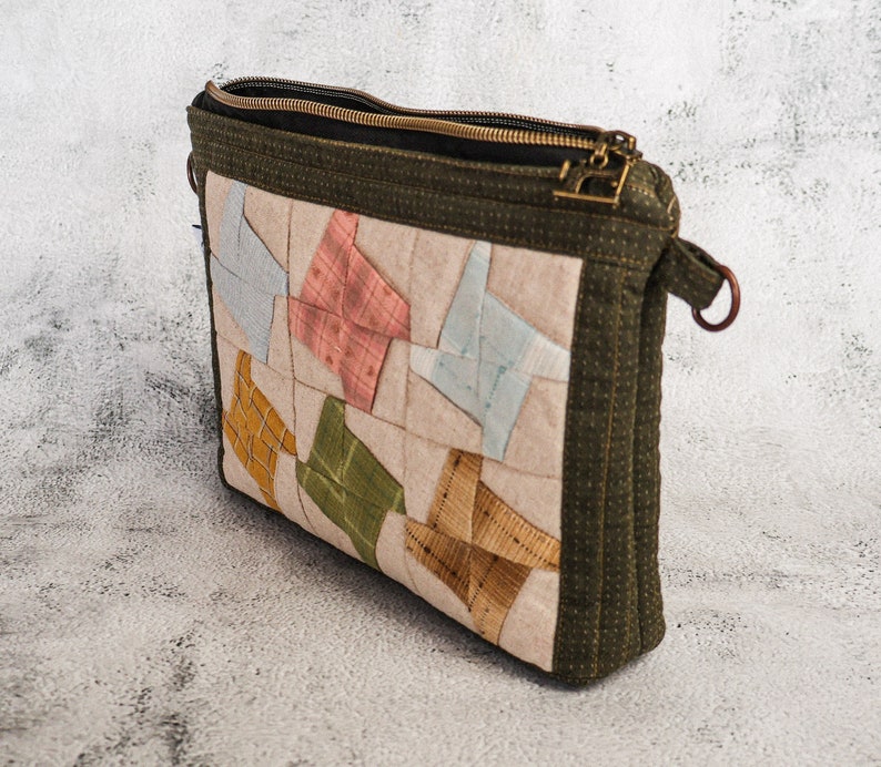 May include: A green quilted zippered pouch with a patchwork design featuring various colours and patterns. The pouch has a brown leather strap.