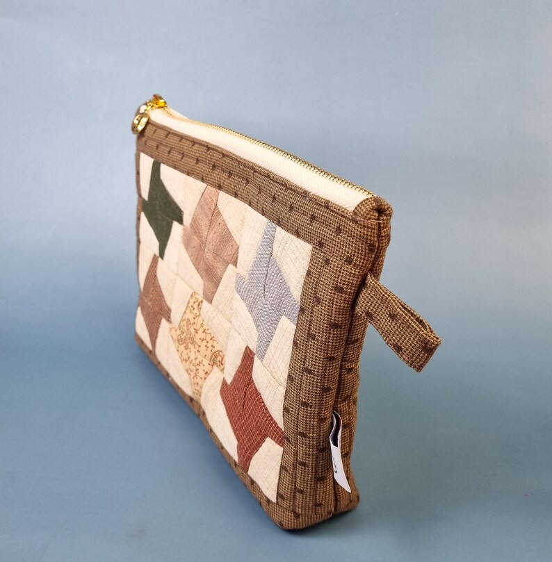 May include: A brown zippered pouch with a patchwork design of various colours and patterns. The pouch has a small brown handle.