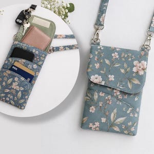May include: A blue crossbody bag featuring a floral pattern with pink and white blossoms and green leaves. The bag has a flap closure, a detachable strap with silver metal clips, and interior pockets containing a wallet, keys, and credit cards.