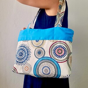 Peut inclure: Un sac cabas bleu et blanc avec un motif mandala color&eacute;. Le sac est doubl&eacute; de tissu bleu et poss&egrave;de deux anses en tissu.