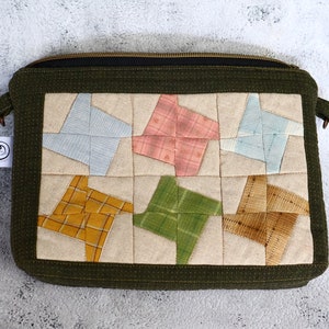 May include: A green zippered pouch with a patchwork design featuring six colourful star-shaped fabric pieces. The pouch is made of a soft, textured fabric and has a zipper closure.