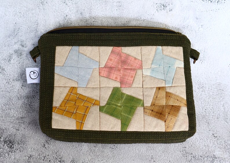 May include: A green zippered pouch with a patchwork design featuring six colourful star-shaped fabric pieces. The pouch is made of a soft, textured fabric and has a zipper closure.
