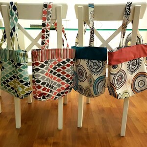 Peut inclure: Quatre sacs fourre-tout en tissu &agrave; motifs diff&eacute;rents. Les sacs sont accroch&eacute;s &agrave; des chaises blanches. Les sacs sont turquoise, rouge, bleu et blanc.