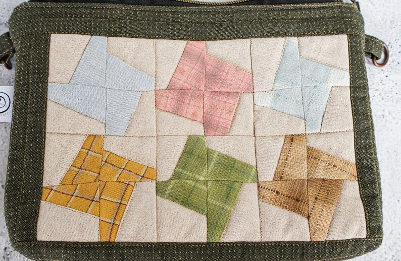 May include: A green fabric zippered pouch with a patchwork design. The front of the pouch is made of beige fabric with six different coloured squares, each with a star-shaped design. The squares are in shades of blue, pink, yellow, green, and brown.