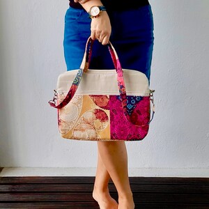 K&ouml;nnte beinhalten: Eine mehrfarbige Patchwork-Tragetasche mit einer beigefarbenen Canvas-Basis. Die Tasche hat einen Rei&szlig;verschluss oben und zwei obere Tragegriffe. Die Tasche ist aus verschiedenen Stoffen mit floralen und Paisley-Mustern in den Farben Rosa, Gelb, Blau und Gr&uuml;n gefertigt.