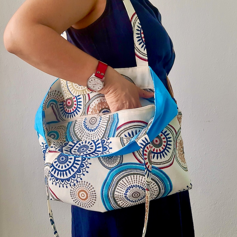 Peut inclure: Un sac fourre-tout &agrave; motifs blancs et bleus avec une doublure bleue. Le sac a une longue bandouli&egrave;re et est port&eacute; &agrave; l'&eacute;paule.
