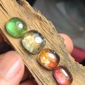 K&ouml;nnte beinhalten: Vier runde, facettierte Edelsteine in verschiedenen Farben, darunter Gr&uuml;n, Gelb, Orange und Pink, werden auf einem St&uuml;ck Holz gezeigt.