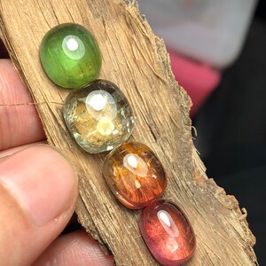 K&ouml;nnte beinhalten: F&uuml;nf ovale Edelsteine in verschiedenen Schattierungen von Gr&uuml;n, Gelb, Orange und Rosa. Die Steine sind in einer Reihe auf einem St&uuml;ck Holz angeordnet.